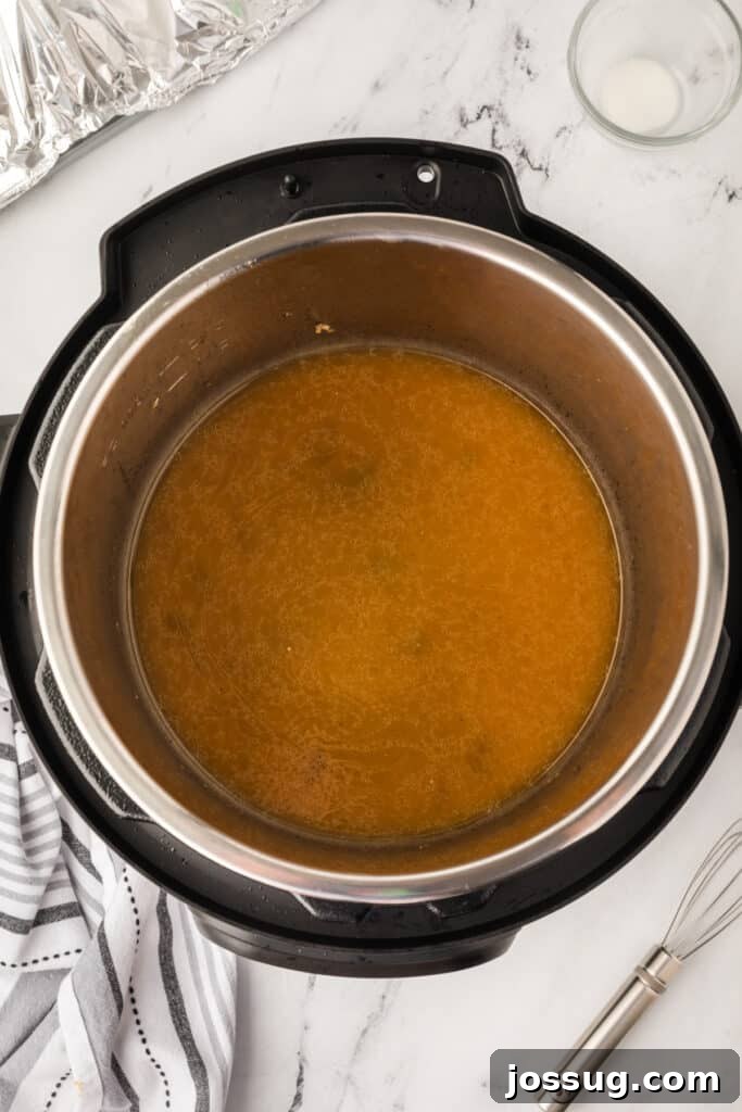 Instant Pot filled with simmering brown gravy after thickening, whisk placed nearby on the counter.