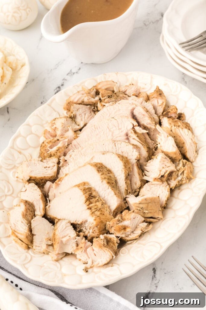 Sliced Instant Pot turkey breast arranged on a white platter with a gravy boat, mashed potatoes, and stacked plates nearby.