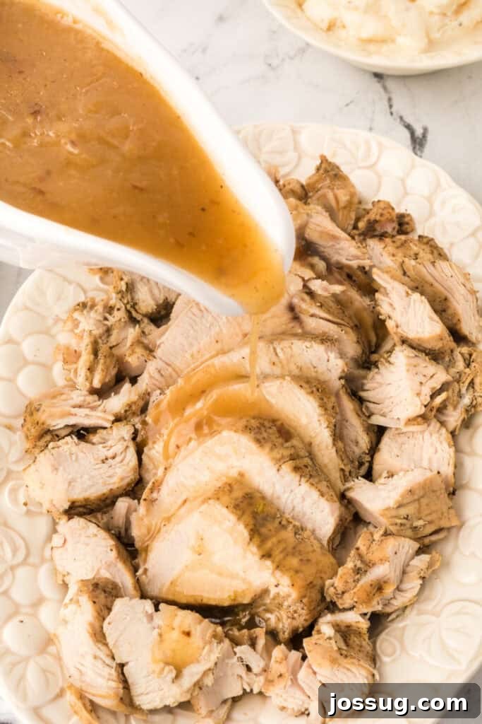 Gravy being poured over sliced turkey breast on a white serving platter for a cozy dinner presentation.
