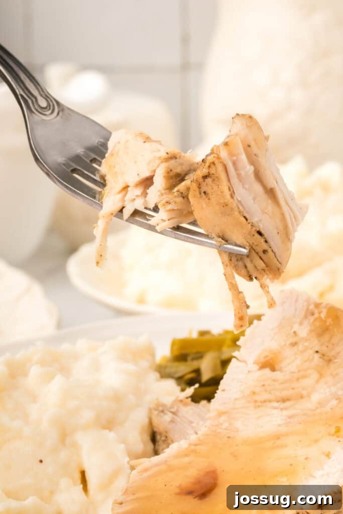 Fork lifting a bite of tender turkey breast with mashed potatoes and green beans blurred in the background.