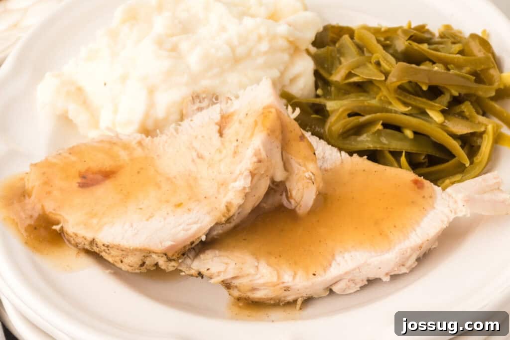 Close-up of sliced turkey breast topped with gravy, served with mashed potatoes and green beans on a white dinner plate.