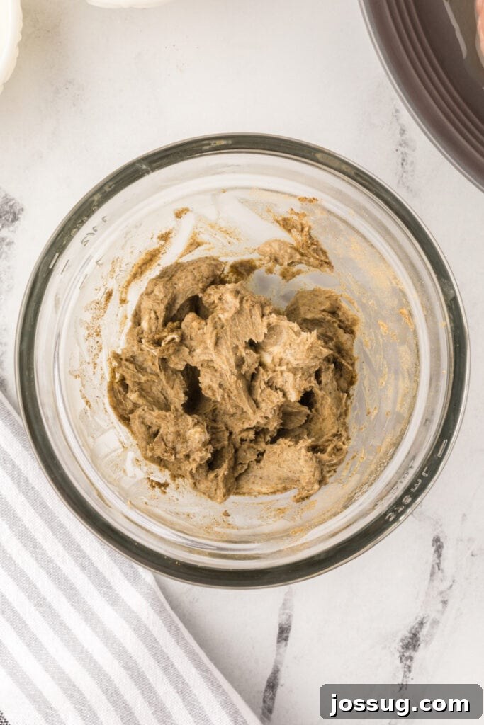 Mixed butter and seasoning forming a smooth herb butter in a glass bowl for turkey coating.