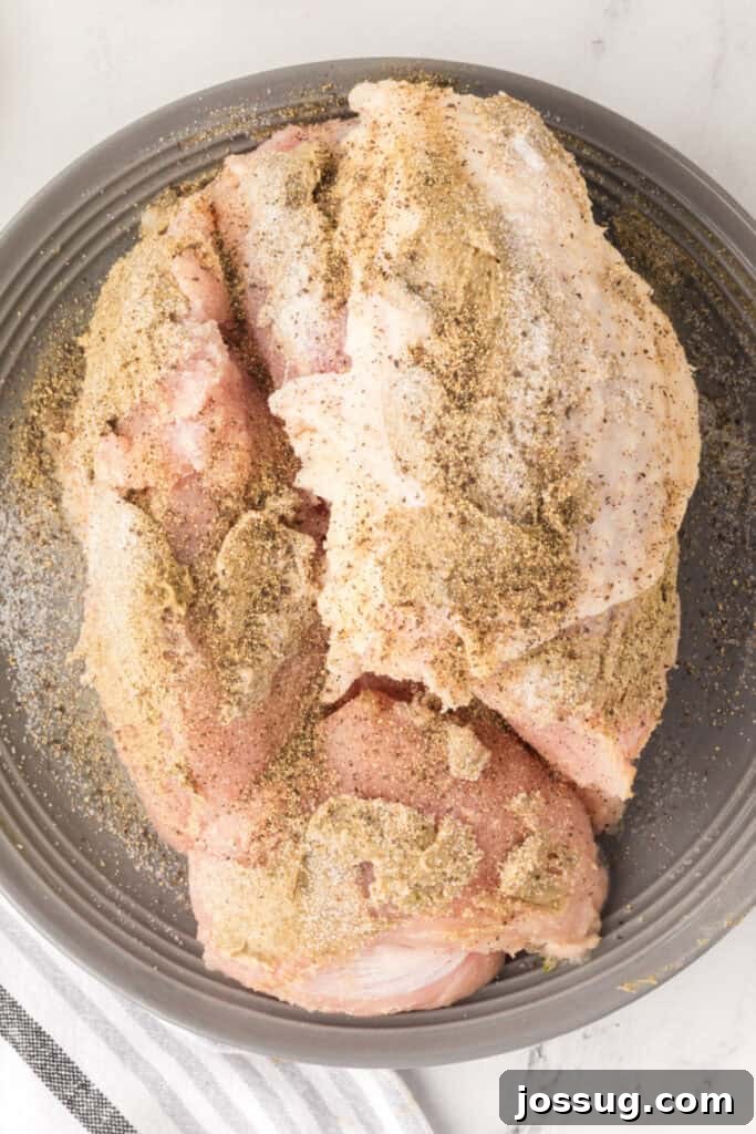 Seasoned turkey breast sprinkled with salt and pepper on a gray plate before searing.