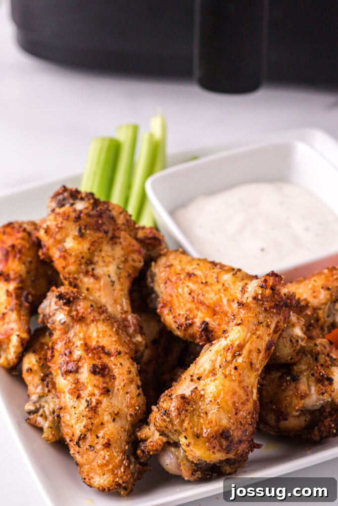 A platter of golden-brown air fryer chicken wings served with fresh carrots, celery sticks, and a creamy dipping sauce.