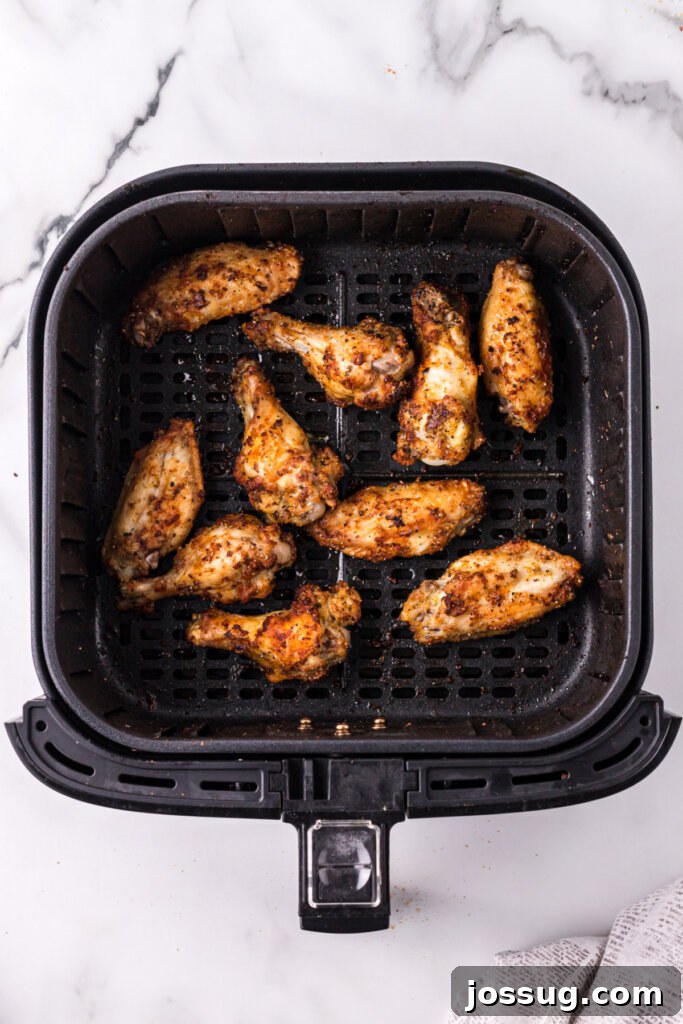 Close-up of golden-brown chicken wings in an air fryer basket, showcasing their crispy texture.