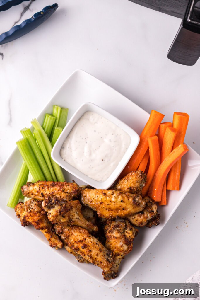 An overhead shot of a generous platter of crispy air fryer chicken wings, accompanied by fresh celery sticks, carrot sticks, and a small bowl of creamy dipping sauce.