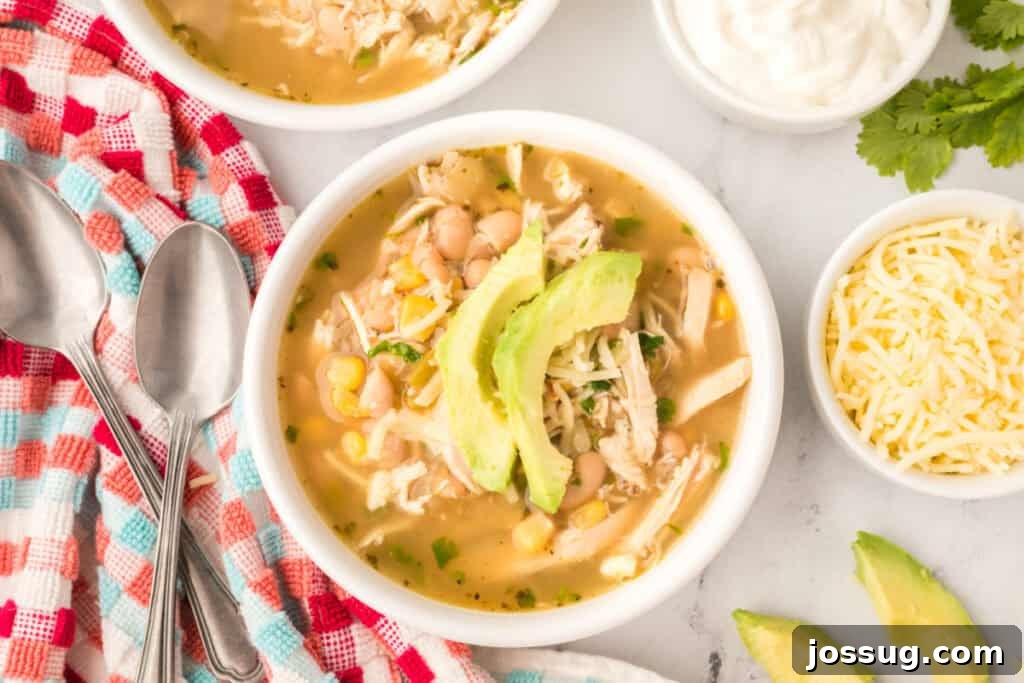 Hearty White Chicken Chili 13 Two bowls of White Chicken Chili with avocado and cheese toppings, surrounded by small bowls of sour cream and shredded cheese.