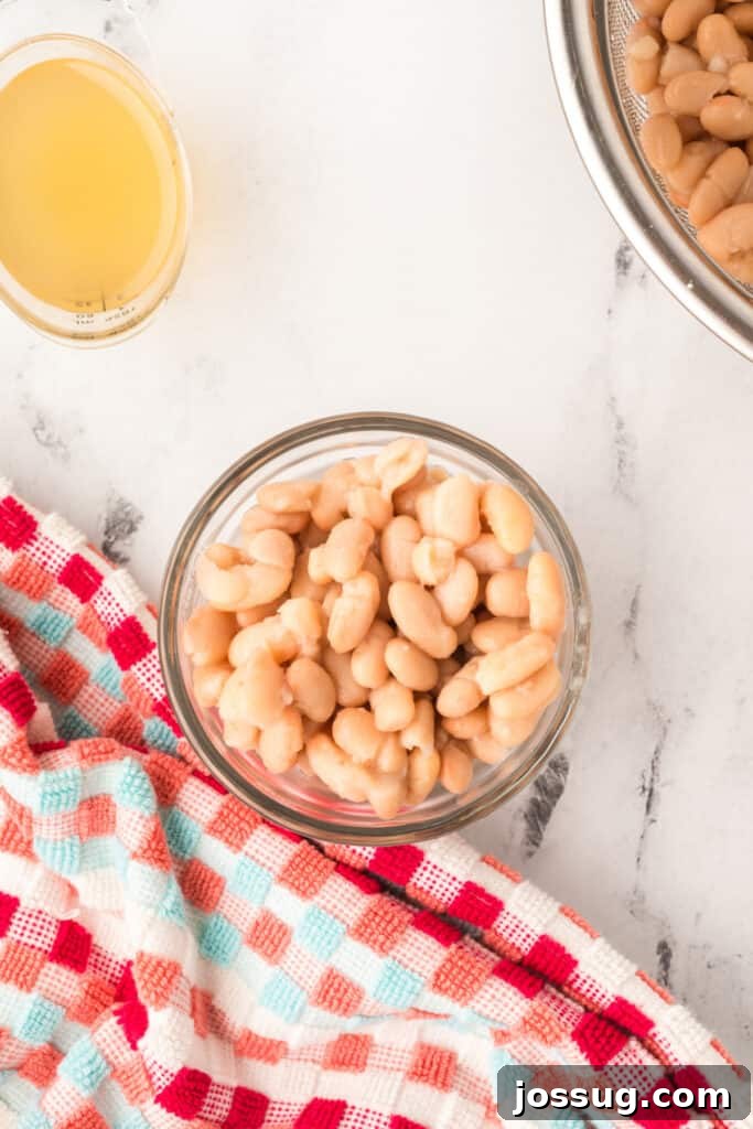 Hearty White Chicken Chili 7 Bowl of rinsed white beans sitting beside a measuring cup of broth on a checkered towel.