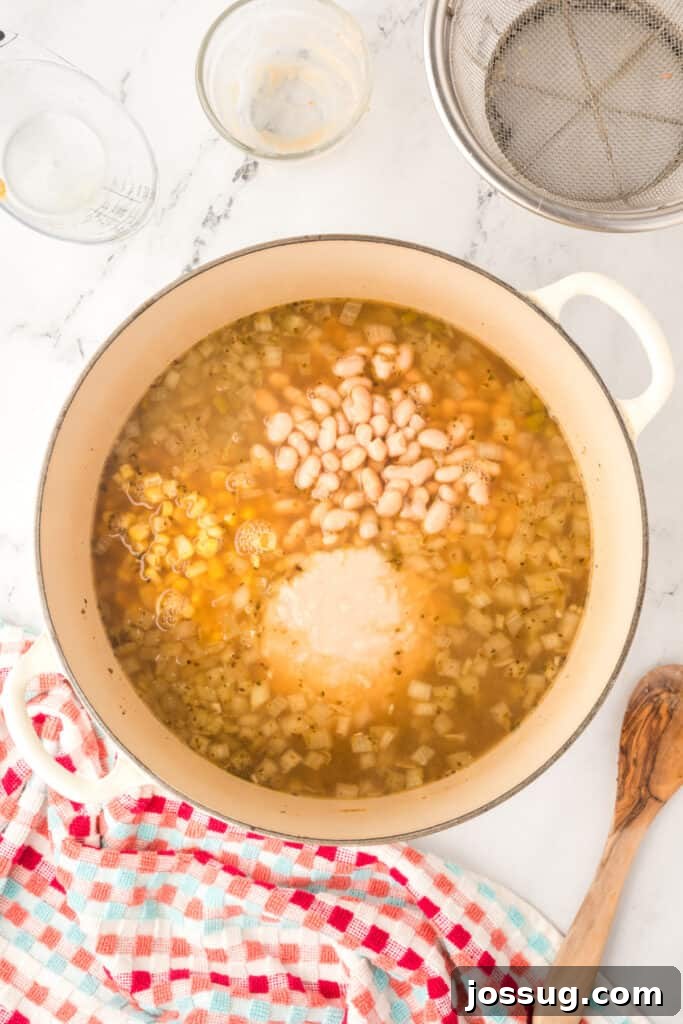 Hearty White Chicken Chili 9 Dutch oven filled with simmering broth, corn, whole beans, and pureed beans combined.