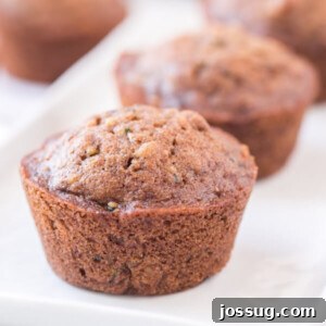 A stack of golden-brown zucchini muffins on a white plate, showcasing their moist texture and spiced goodness.