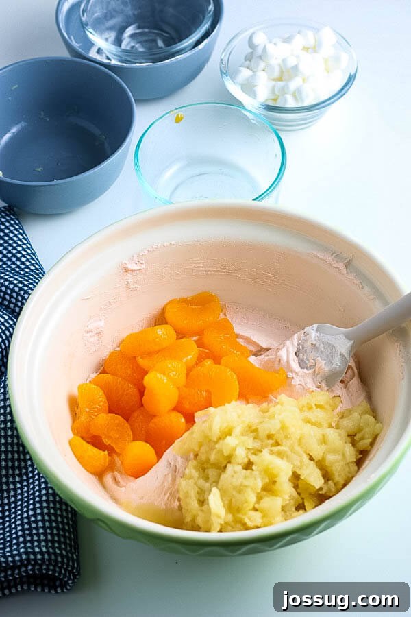 Creamsicle Dream Dessert 6 oranges and pineapple added to fluff salad mixture in a mixing bowl