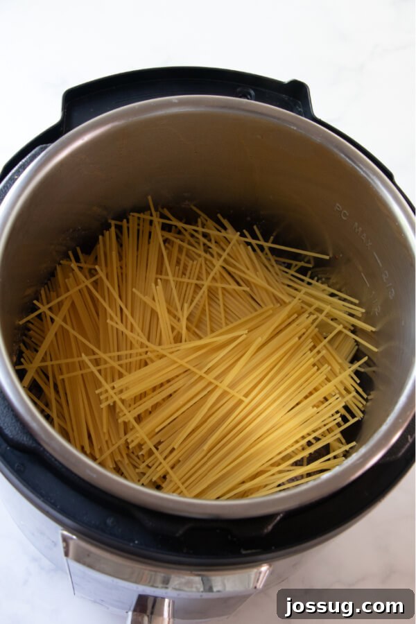 Uncooked spaghetti noodles carefully layered on top of the browned meat in the Instant Pot.
