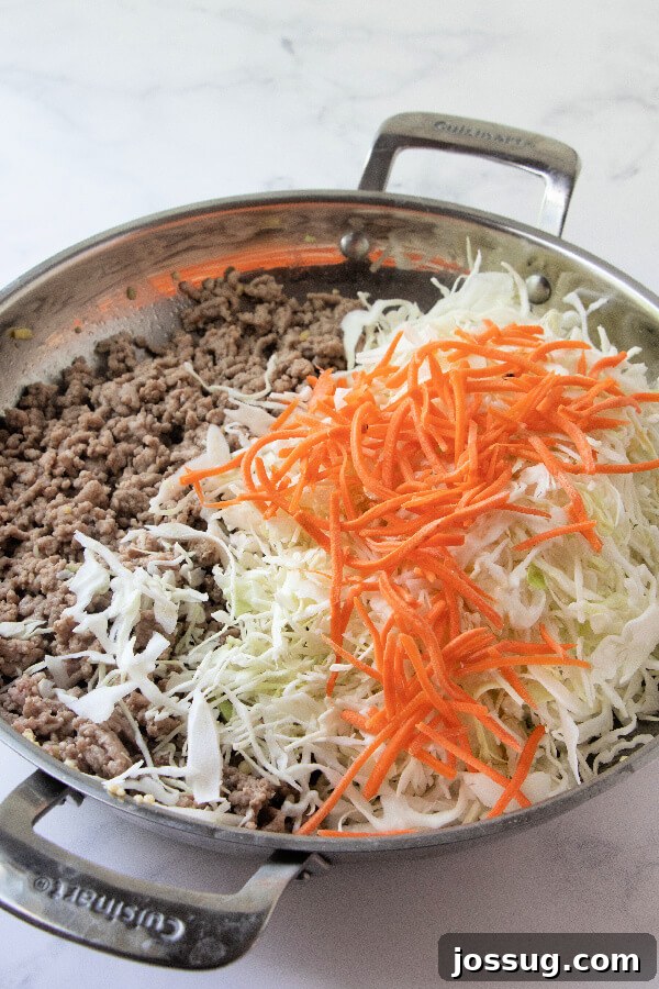 Adding Vegetables to Egg Roll in a Bowl Shredded cabbage and carrots being added to the skillet with cooked ground meat and aromatics.