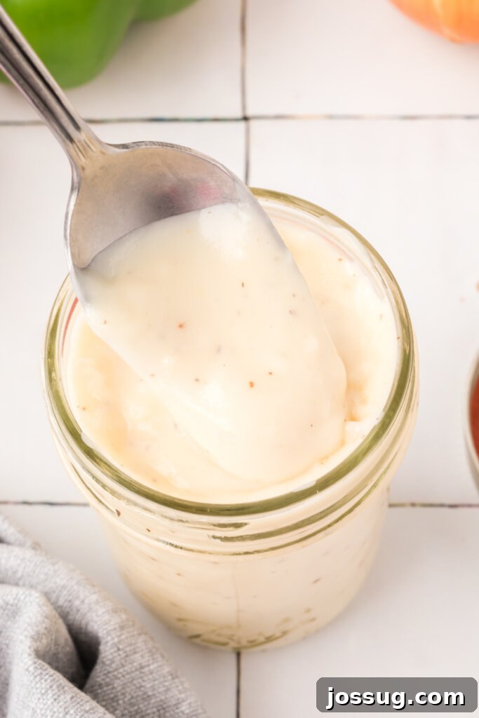 A spoon scooping creamy homemade condensed cream soup substitute out of a glass jar, emphasizing its rich texture.