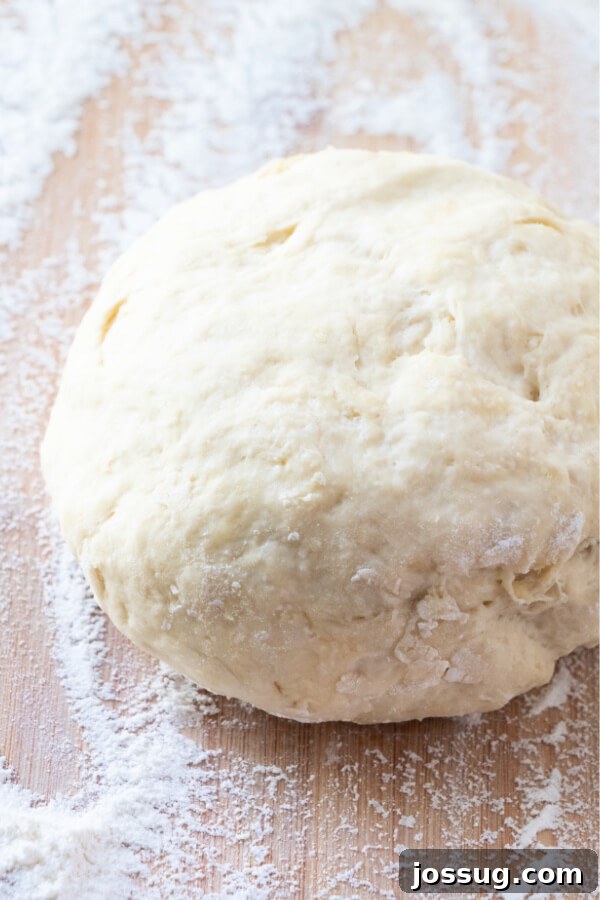 A perfectly proofed ball of homemade pizza dough, resting on a lightly floured surface, ready to be shaped and baked.