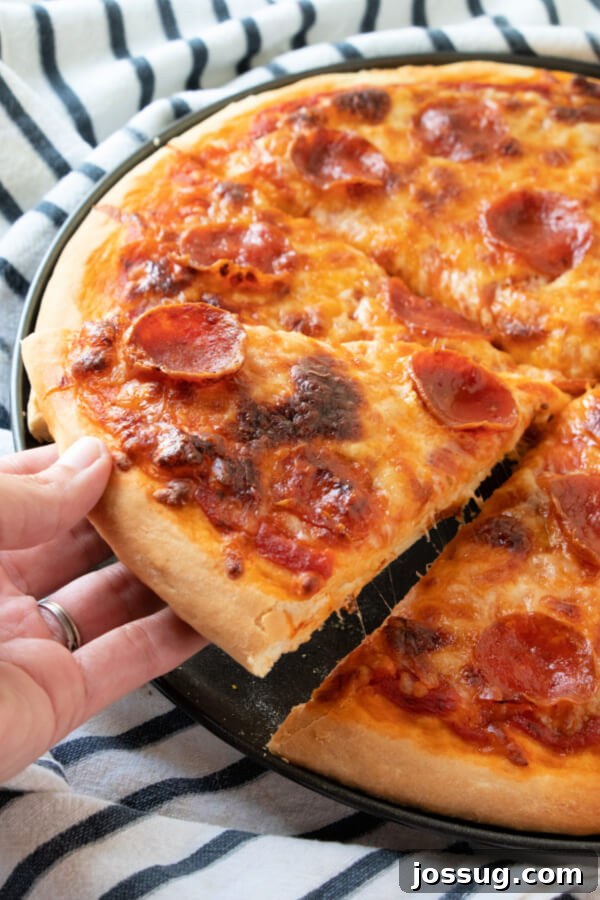A hand reaching for a slice of freshly baked homemade pizza, showing off the perfectly golden and bubbly crust with melted cheese and pepperoni.