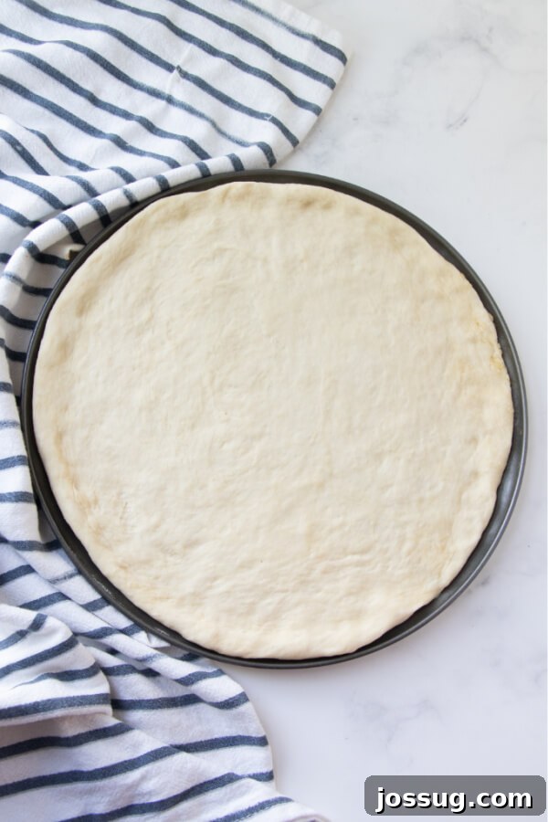 Freshly shaped pizza dough beautifully pressed out into a round pizza pan, glistening with a hint of olive oil, eagerly awaiting its sauce and delicious toppings.