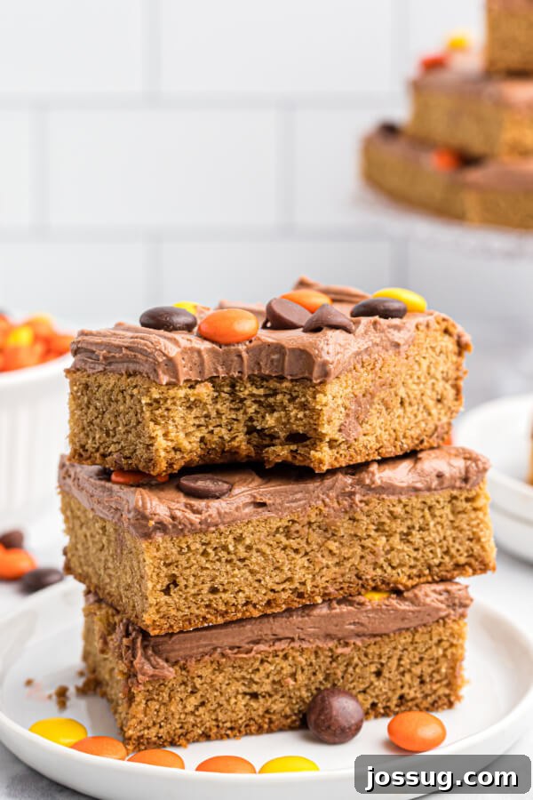Three perfectly thick, soft, and chewy peanut butter cookie bars stacked neatly on a pristine white plate, showcasing their inviting texture.