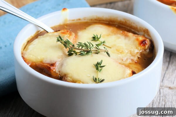Golden Gratin French Onion Soup 10 A ceramic bowl of French Onion Soup with a spoon resting inside, showing the melted cheese and a glimpse of the rich broth.