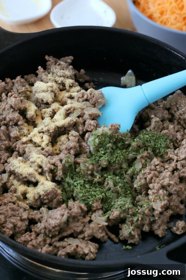 One-Pot Cheesy Beef Mac 5 Seasonings, including dried parsley and garlic powder, being added to the browned ground beef in a skillet.