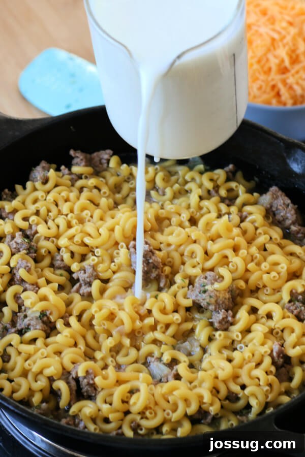 One-Pot Cheesy Beef Mac 6 Adding uncooked elbow macaroni and milk to the skillet with browned ground beef.