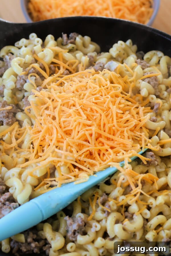 One-Pot Cheesy Beef Mac 7 Shredded cheddar cheese being stirred into the creamy macaroni and ground beef mixture.