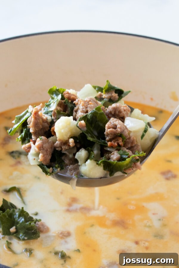 A ladle filled with creamy Zuppa Toscana soup, being lifted from a pot, ready to be served.