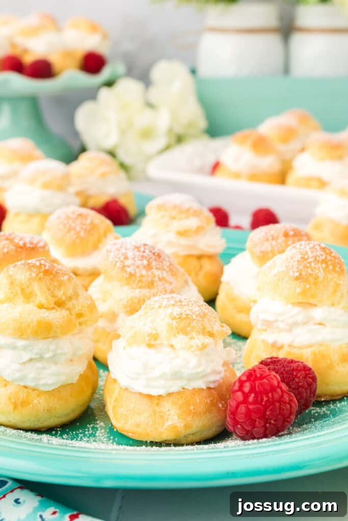 Pillowy Cream Dreams 2 Several golden cream puffs arranged beautifully on a teal plate with fresh raspberries scattered around, inviting a delightful indulgence.