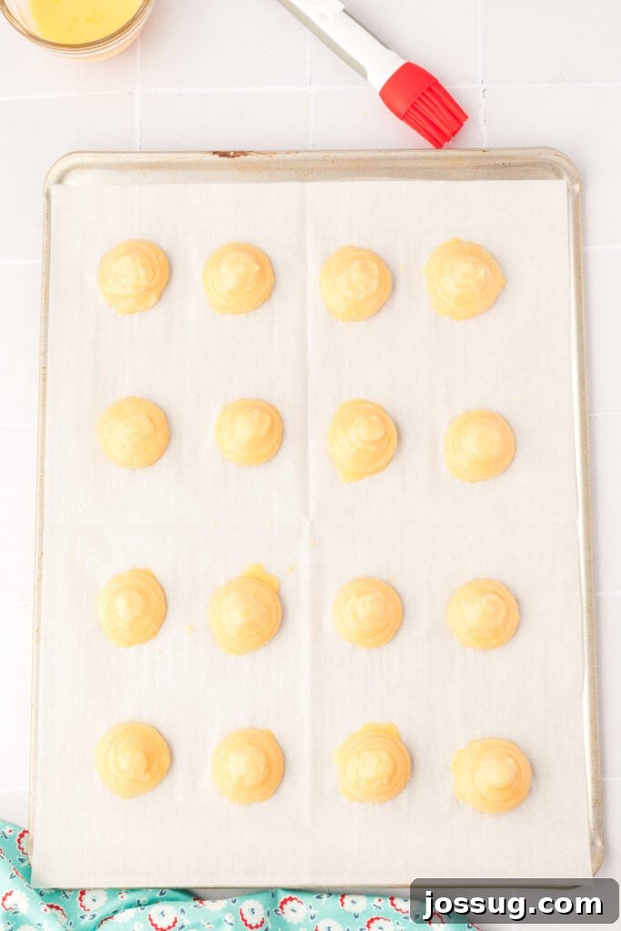 Pillowy Cream Dreams 13 Preheat oven to 375°F. Transfer the dough mixture to a large disposable decorator pastry bag fitted with a large round tip. Line a baking sheet with parchment paper. Pipe circles 1-½ inch round onto parchment paper. Moisten your finger with water and gently smooth out the pointed peaks, if necessary. Brush the pastry with egg wash.