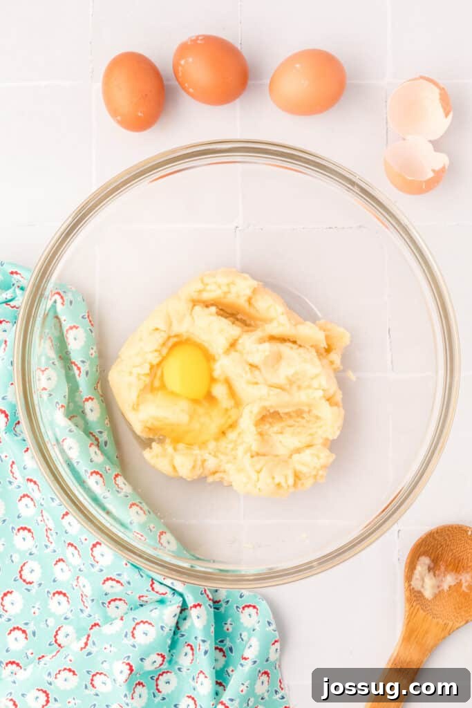 Pillowy Cream Dreams 10 Add 4 eggs, one at a time, into the cooled dough, stirring to incorporate each egg completely before adding the next egg to achieve the perfect consistency.