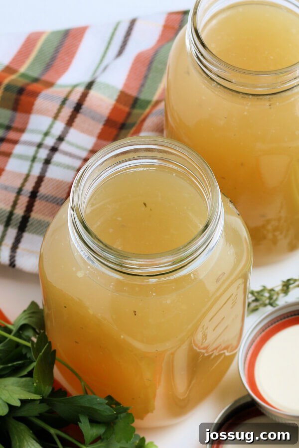 Rich Homemade Turkey Stock 5 Multiple glass jars filled with homemade turkey stock, arranged artfully with fresh vegetables and herbs around them.
