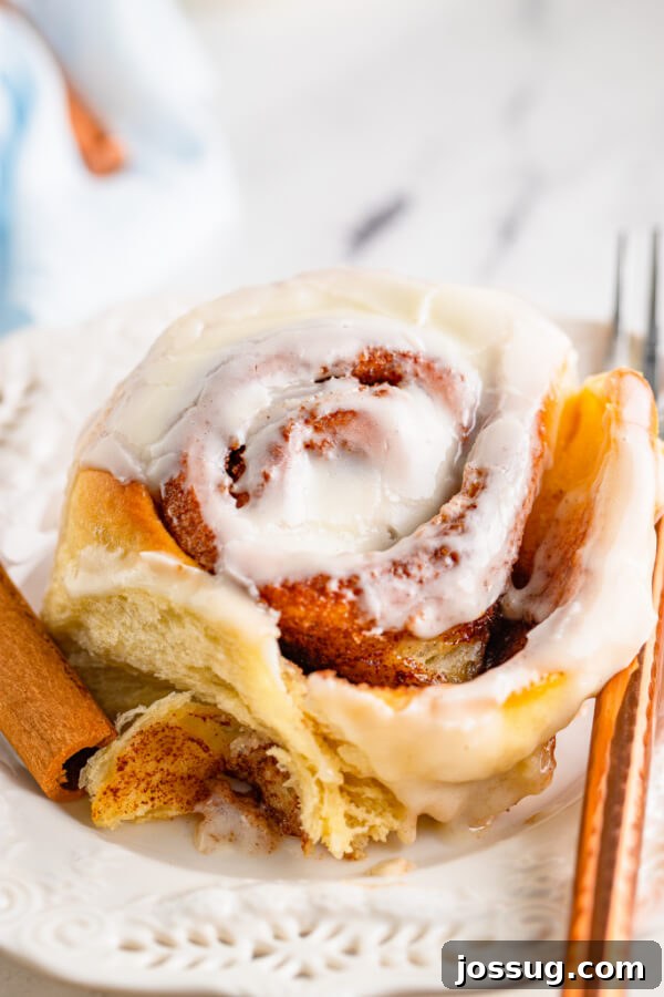 Gooey homemade cinnamon roll on a plate, topped with cream cheese frosting.