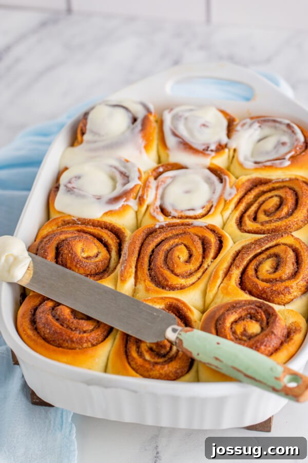 Applying cream cheese frosting to warm, freshly baked cinnamon rolls.