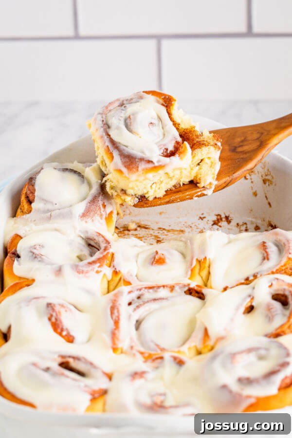 A single homemade cinnamon roll on a wooden spatula, showcasing its gooey layers and frosting.