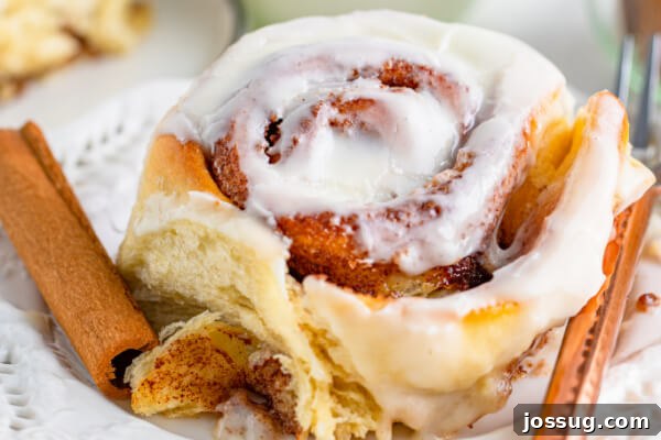 A beautifully frosted cinnamon roll on a white plate, ready to be enjoyed.