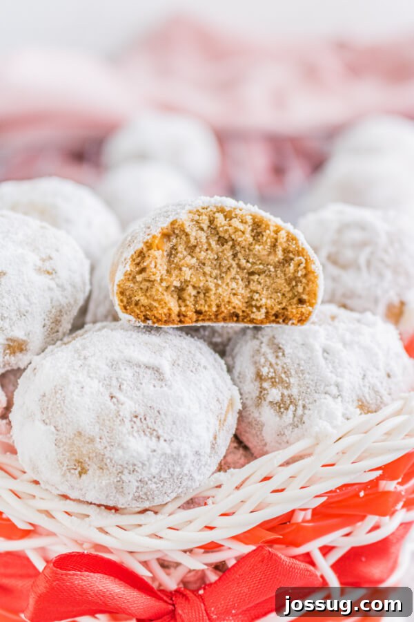 A festive holiday basket filled with stacked Gingerbread Pecan Snowball cookies, with one cookie cut in half to reveal its tender, spiced interior and crunchy pecans.