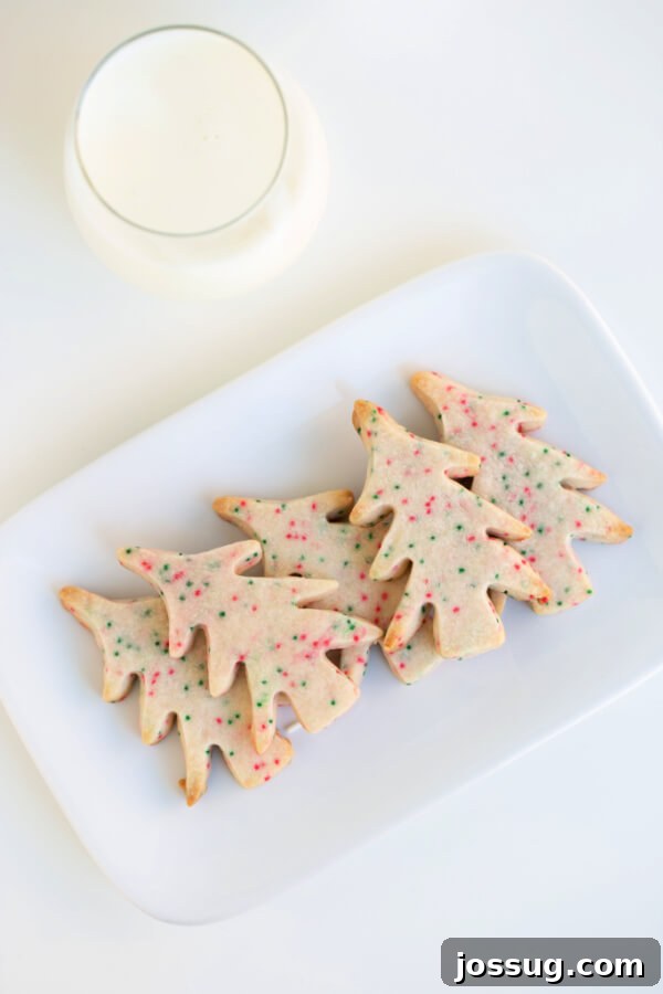 Close-up of tree-shaped Christmas shortbread cookies on a white plate, showcasing their festive sprinkles.
