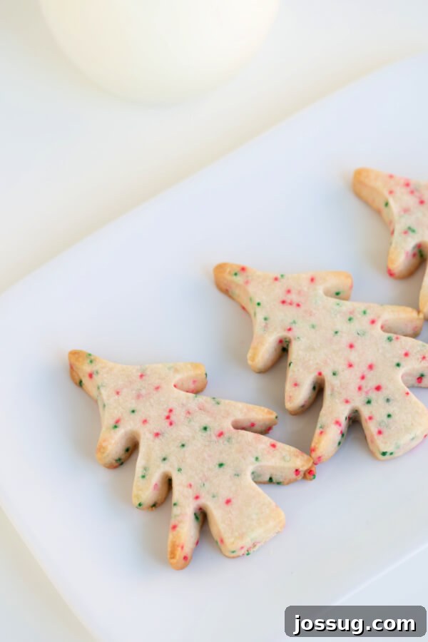 Closeup of tree-shaped shortbread cookies on a white plate, showing the detailed texture and festive sprinkles.