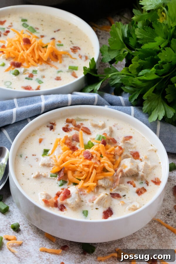 Creamy Chicken Bacon Ranch Delight 9 Two steaming bowls of Chicken Bacon Ranch Soup, garnished and ready to be served, on a rustic wooden surface.