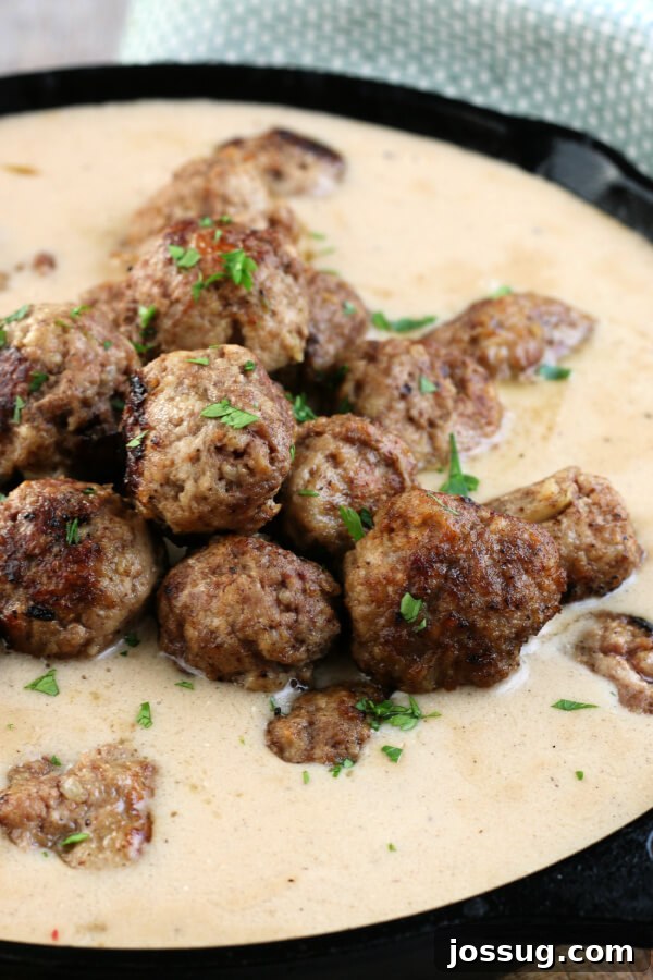 Perfectly cooked Swedish Meatballs simmering in a rich, brown sour cream gravy within a large pan.