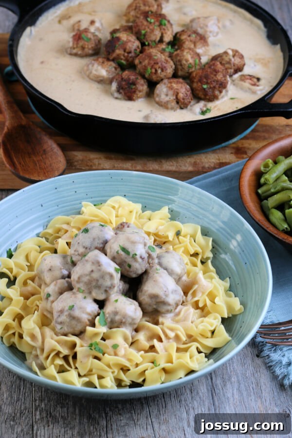 A beautifully presented serving of Swedish Meatballs and gravy in the foreground, with the pan of additional meatballs simmering in the background, ready for serving.