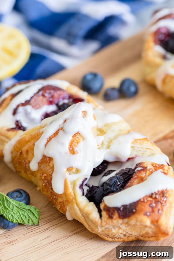 Bright Lemon Blueberry Danish Delight 30 Golden lemon blueberry danish on a rustic wooden board, garnished with fresh blueberries and a blue linen napkin