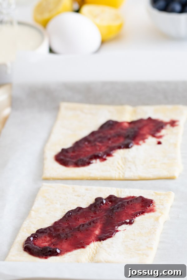 Bright Lemon Blueberry Danish Delight 4 Spreading sweet blueberry jam evenly over a sheet of puff pastry dough, a key step in preparing the Danish filling