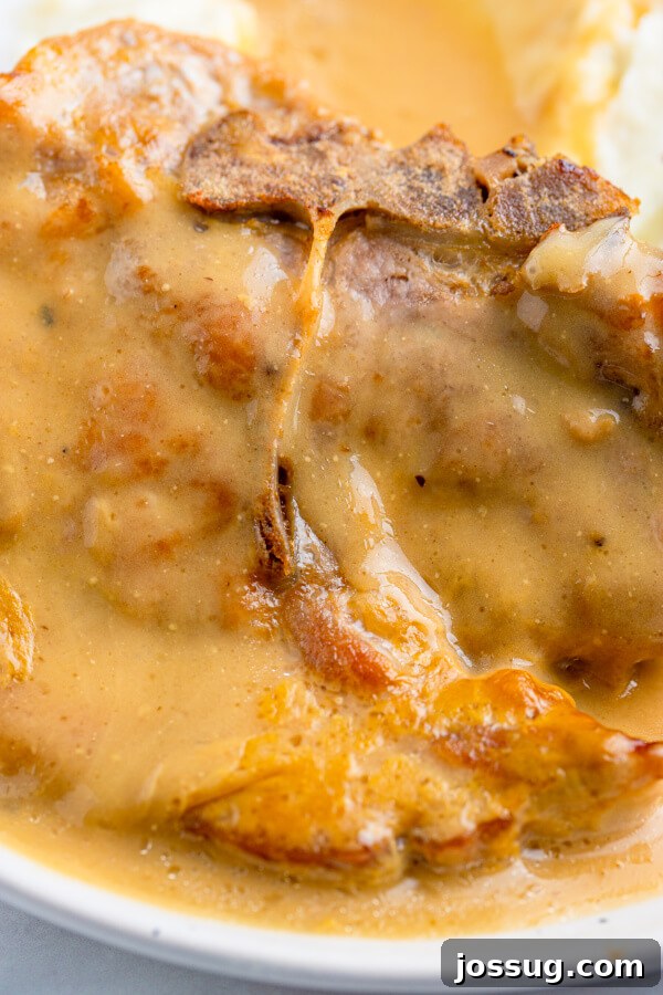 Tender Baked Pork Chops in Rich Pan Gravy 6 Baking dish filled with pork chops submerged in gravy, covered with foil, in the oven