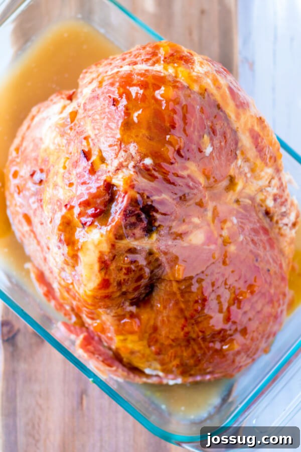 A spiral ham generously coated with the apricot dijon glaze, placed in a roasting pan before being transferred to the oven for baking.