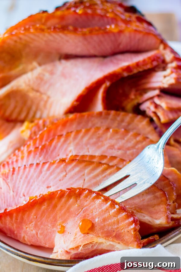 A close-up shot of a fork picking up a succulent slice of Apricot Dijon Spiral Ham, highlighting its juicy texture and caramelized glaze.