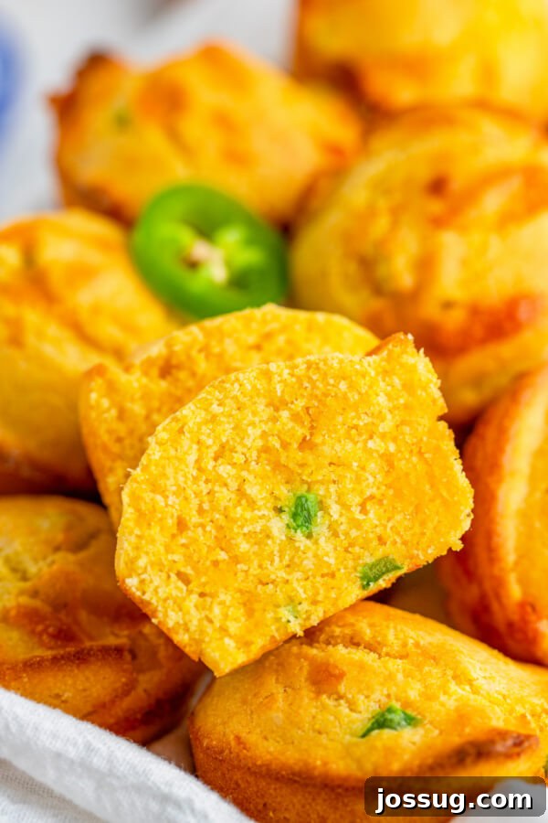 A close-up view of a Jalapeño Cheddar Corn Muffin cut in half, revealing the moist interior with visible chunks of melted cheddar cheese and finely diced jalapeños.