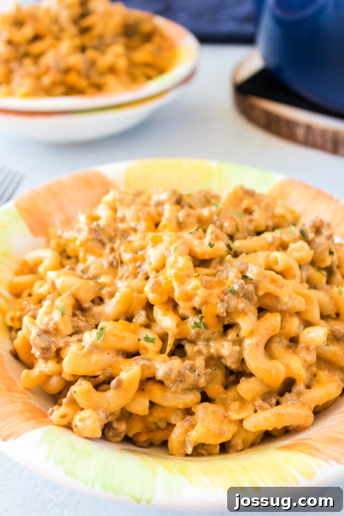 A large bowl of hearty cheeseburger pasta sits on a rustic wooden table, garnished with fresh parsley, surrounded by smaller serving dishes.