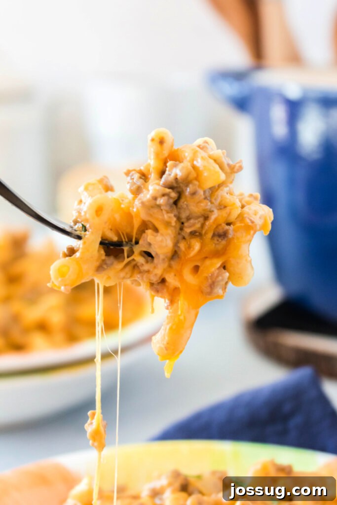 A fork laden with cheesy, creamy cheeseburger pasta, showing the delicious texture and melted cheese strands, inviting a bite.