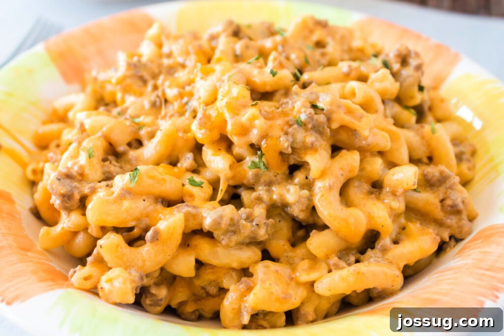 A generous serving of one-pot cheeseburger pasta in a white bowl, garnished with green onions, resting on a clean wooden surface.